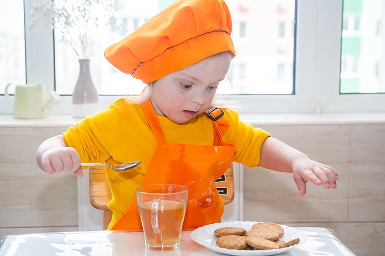 Girl cooking biscuits dressed in orange clothes and hat.